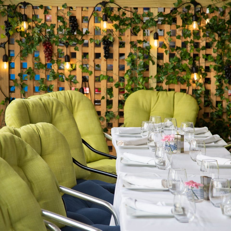 Alihan's Mediterranean Cuisine dining area with set tables, green chairs, and a vine-covered wooden trellis.