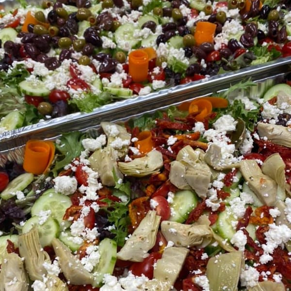 Two large trays of Mediterranean salad with lettuce, cucumbers, feta, olives, and artichoke hearts.