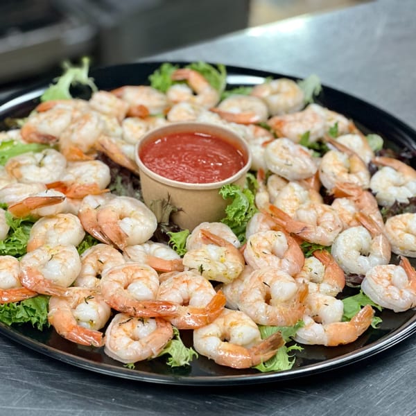 A black platter filled with cooked shrimp on lettuce, surrounding a cup of red cocktail sauce.