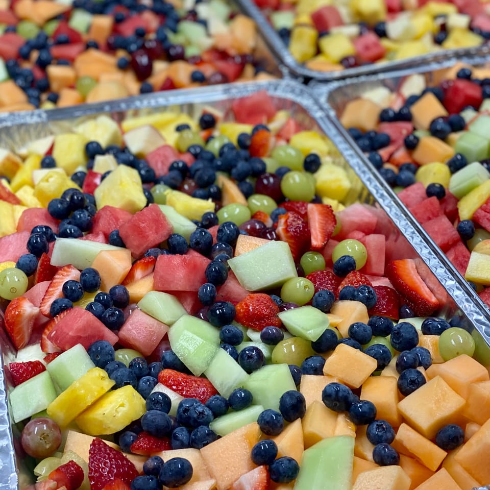 Close-up of several aluminum catering trays filled with colorful diced fresh fruit salad.