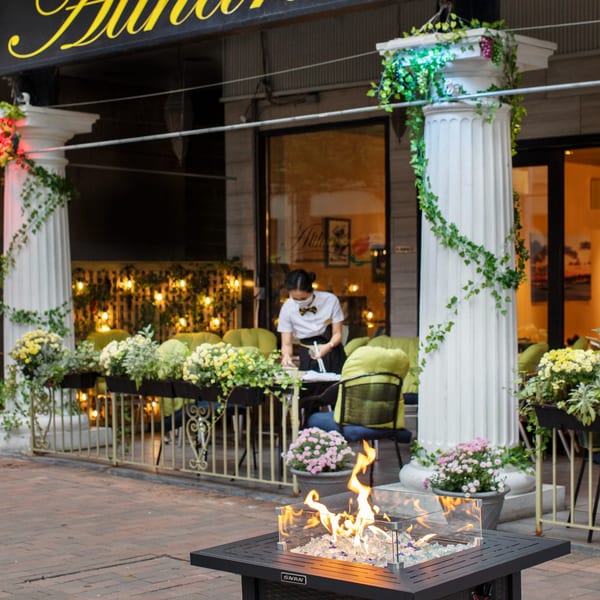 Outdoor patio of Alihan's Mediterranean Cuisine with a fire pit, columns, and a server setting a table.