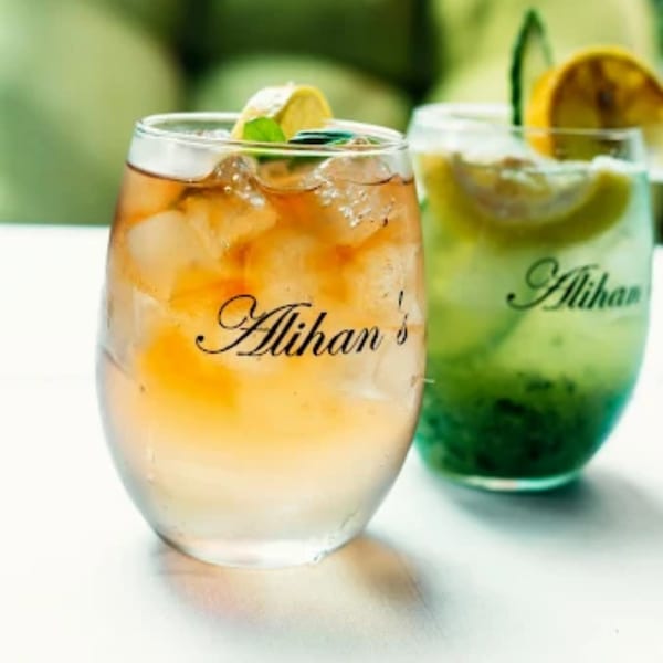 Two refreshing Alihan's drinks, one amber and one green, garnished with citrus and mint.