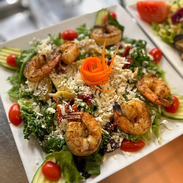 Mediterranean salad with grilled shrimp, feta cheese, cherry tomatoes, cucumbers, and a carrot garnish.