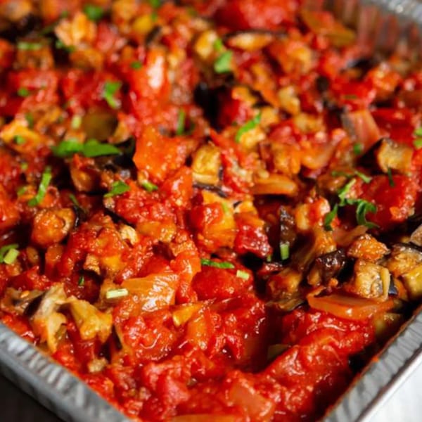 Close-up of a Mediterranean eggplant and tomato dish, garnished with fresh herbs in a foil pan.