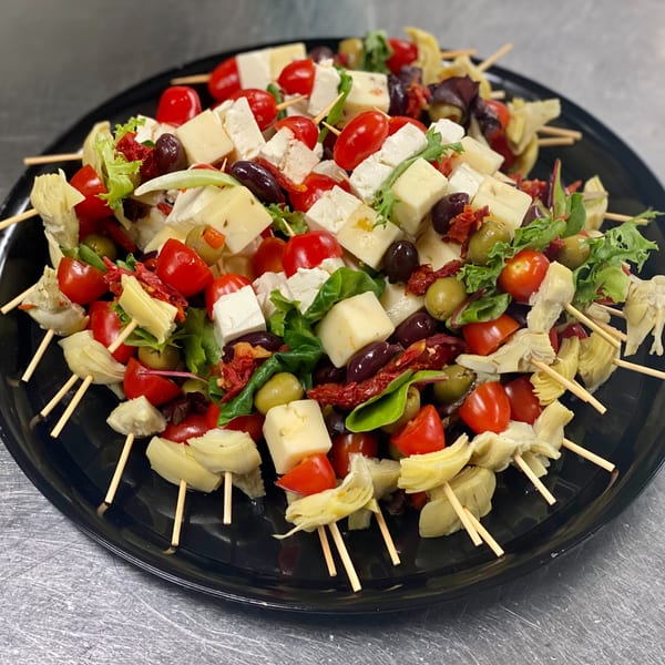 A black platter filled with Mediterranean skewers featuring cheese, tomatoes, olives, and artichoke hearts.