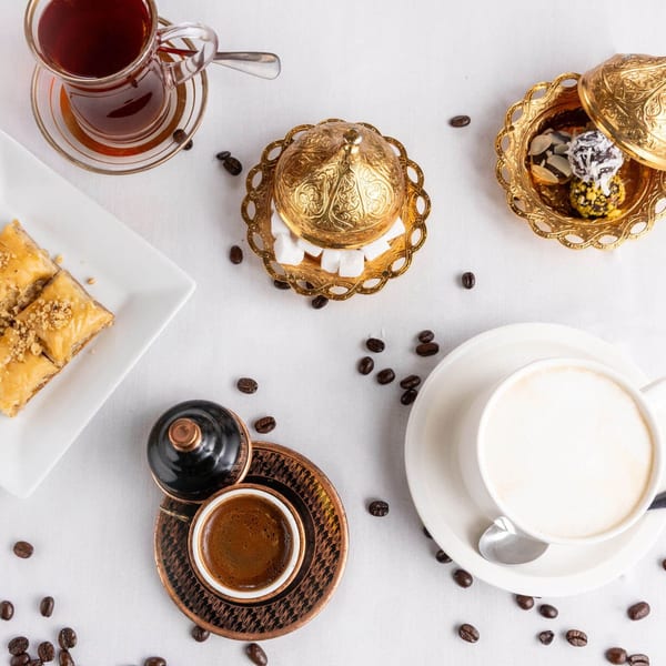 Overhead view of baklava, Turkish coffee, tea, and desserts on a white tablecloth.