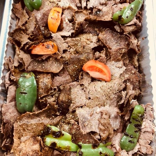 Shaved Mediterranean meat with grilled green peppers and tomato slices in a serving tray.