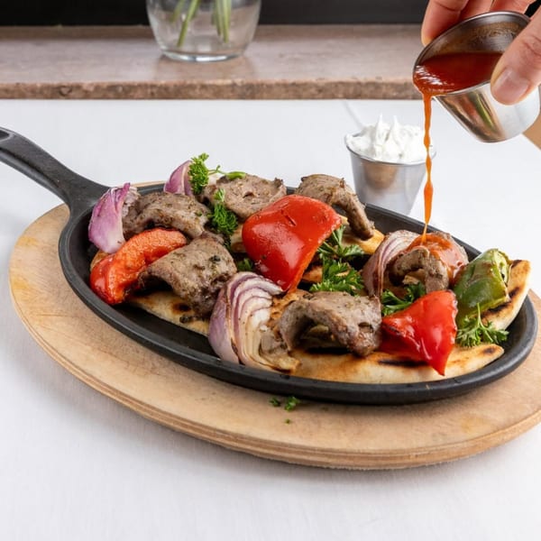 Alihan's Mediterranean Cuisine's sizzling beef and vegetable platter with sauce being poured over it.