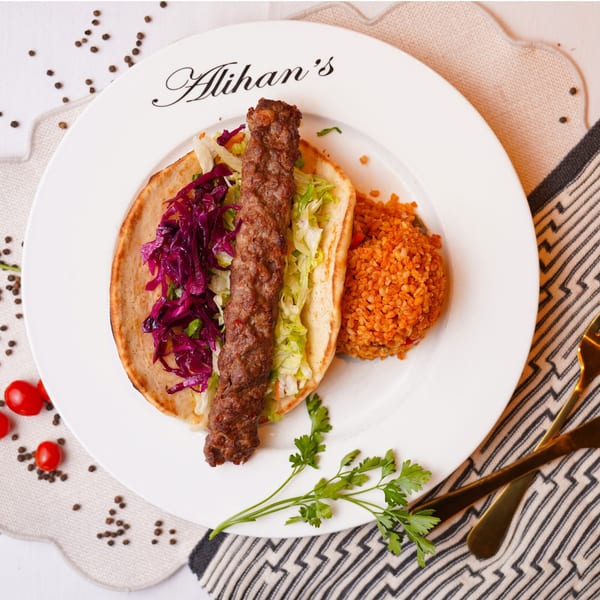 Alihan's Mediterranean Cuisine Adana kebab with red cabbage, lettuce, and bulgur on a white plate.
