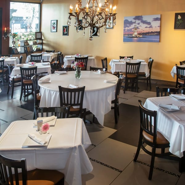 Alihan's Mediterranean Cuisine dining room with white-clothed tables, dark chairs, and a chandelier.