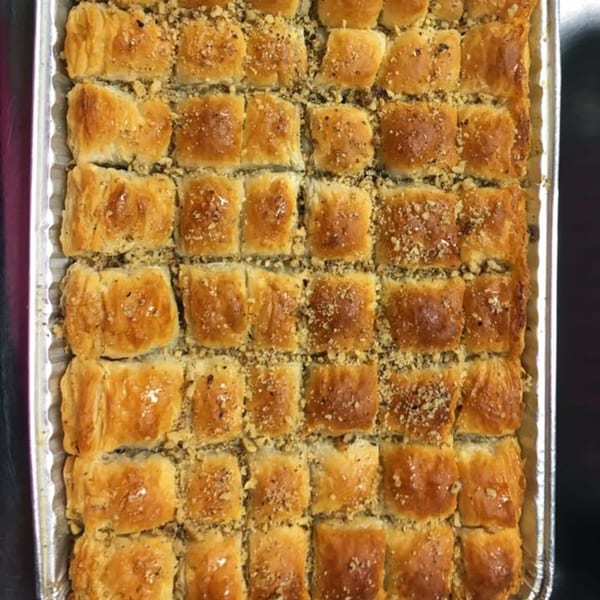 A tray of golden-brown baklava squares, glistening with syrup and sprinkled with chopped nuts.