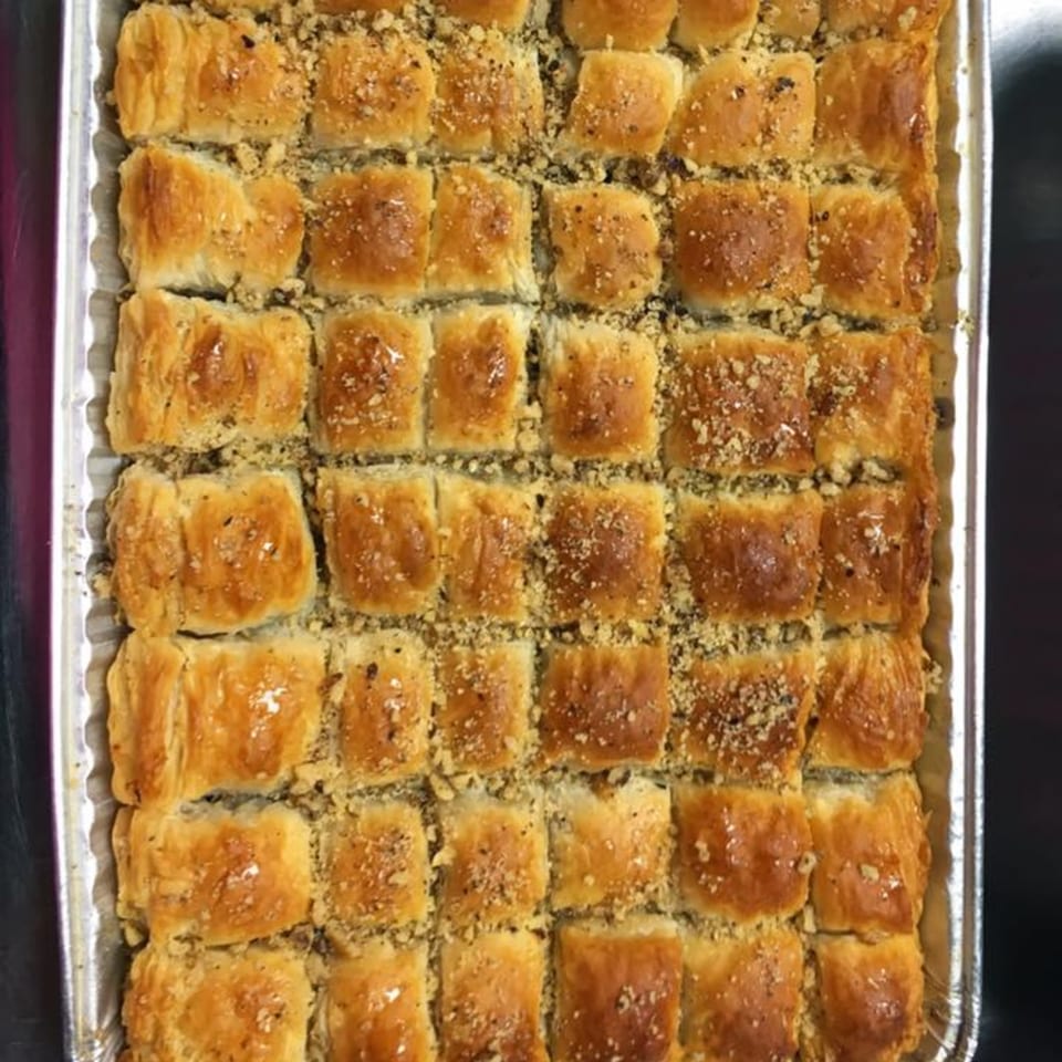 A tray of golden-brown baklava squares, glistening with syrup and sprinkled with chopped nuts.