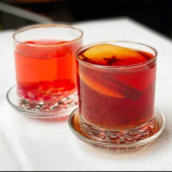 Two glasses of red Mediterranean tea, one with fruit and spices, on a white tablecloth.