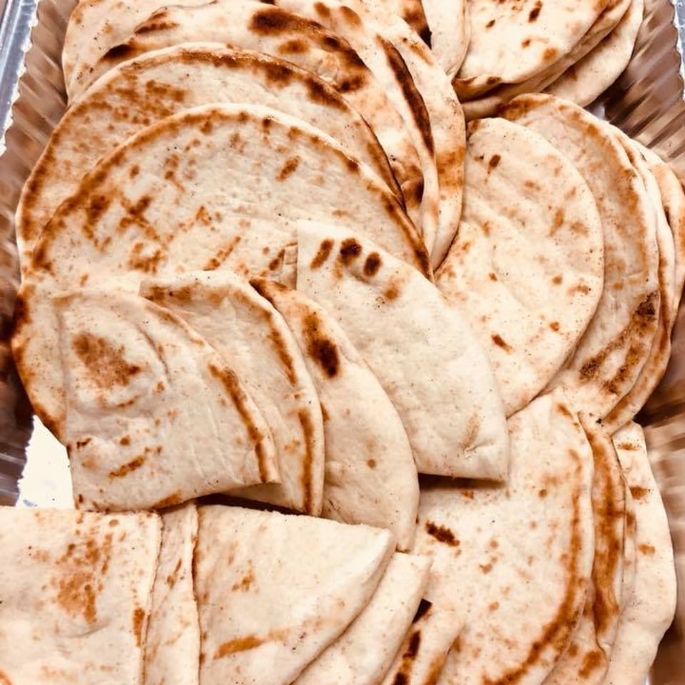 A close-up of several pieces of warm, lightly browned Mediterranean pita bread in a metal tray.