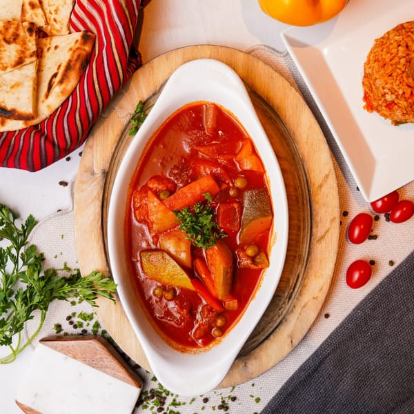 A white dish of Alihan's Mediterranean vegetable stew with flatbread, rice, and tomatoes.