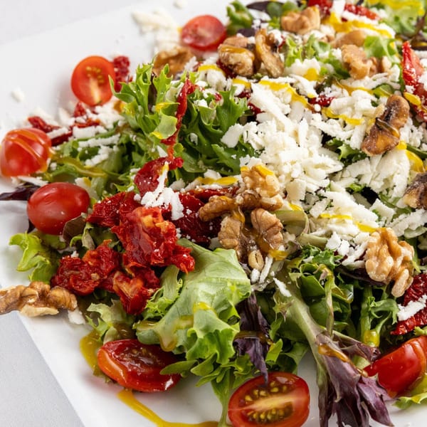Close-up of a vibrant Mediterranean salad with mixed greens, cherry tomatoes, feta, walnuts, and sun-dried tomatoes.