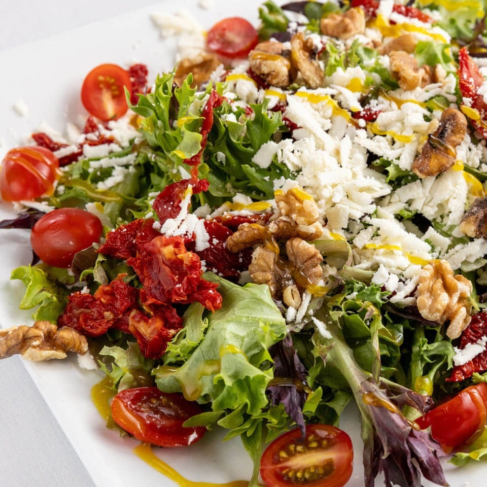 Close-up of a vibrant Mediterranean salad with mixed greens, cherry tomatoes, feta, walnuts, and sun-dried tomatoes.