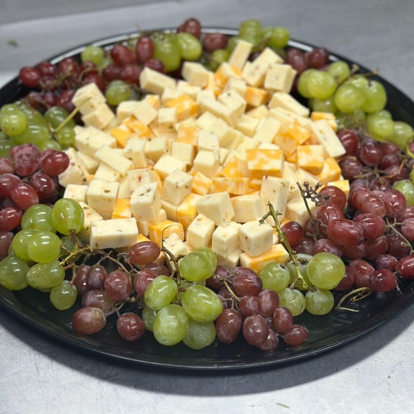 A black platter filled with cubed cheeses, green grapes, and red grapes, ready to be served.