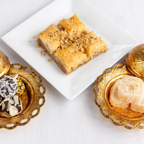 Alihan's Mediterranean baklava and assorted desserts in ornate gold dishes on a white tablecloth.