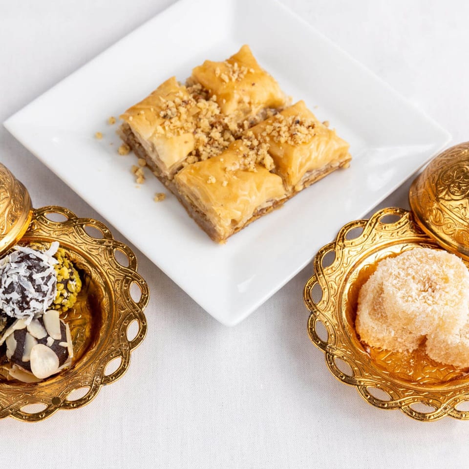 Alihan's Mediterranean baklava and assorted desserts in ornate gold dishes on a white tablecloth.