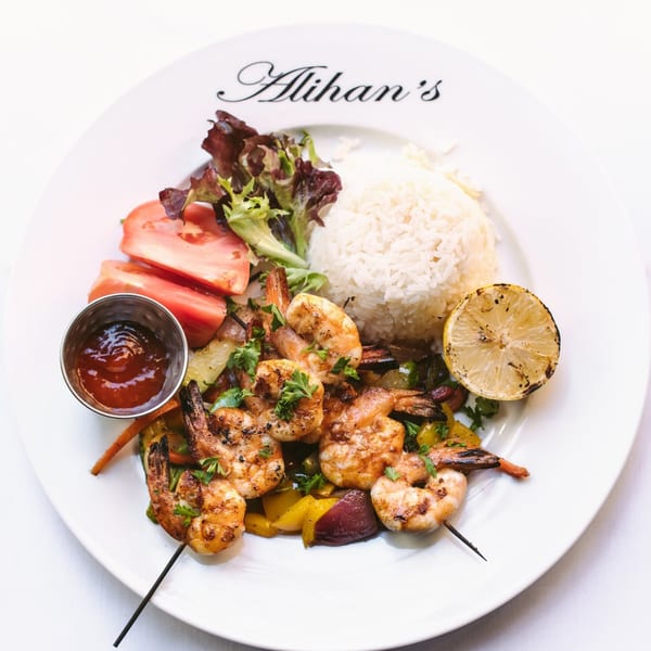 Alihan's grilled shrimp skewers with rice, salad, and a grilled lemon on a white plate.