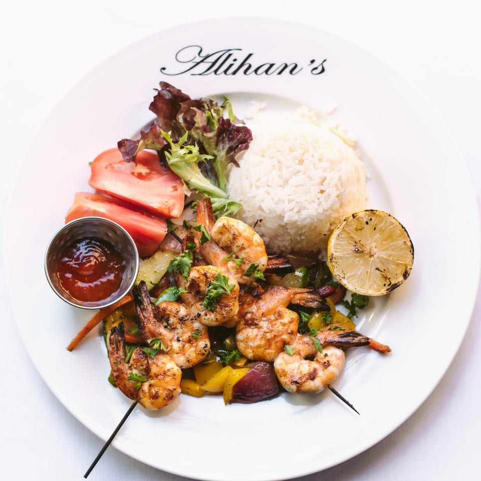 Alihan's grilled shrimp skewers with rice, salad, and a grilled lemon on a white plate.